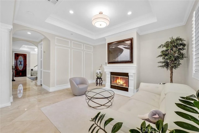living room with crown molding, a raised ceiling, arched walkways, and a glass covered fireplace