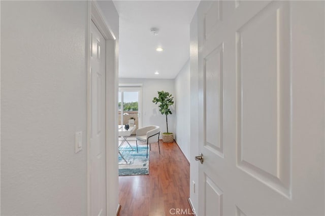 hall featuring a textured wall, wood finished floors, and recessed lighting