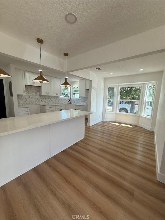 kitchen featuring wood finished floors, a sink, a textured ceiling, decorative light fixtures, and decorative backsplash