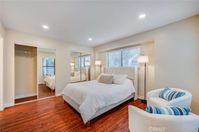 bedroom with multiple windows, two closets, wood finished floors, and baseboards