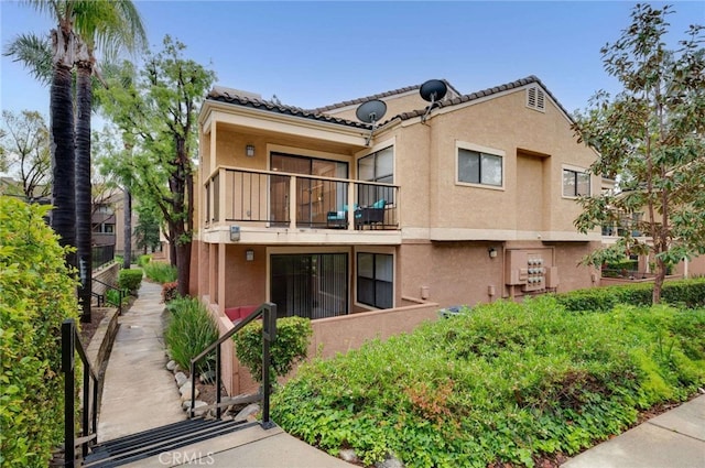 back of property with a balcony, stucco siding, and a tiled roof