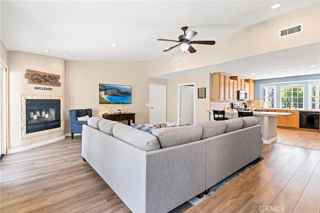living area with light wood-type flooring, ceiling fan, a glass covered fireplace, recessed lighting, and baseboards