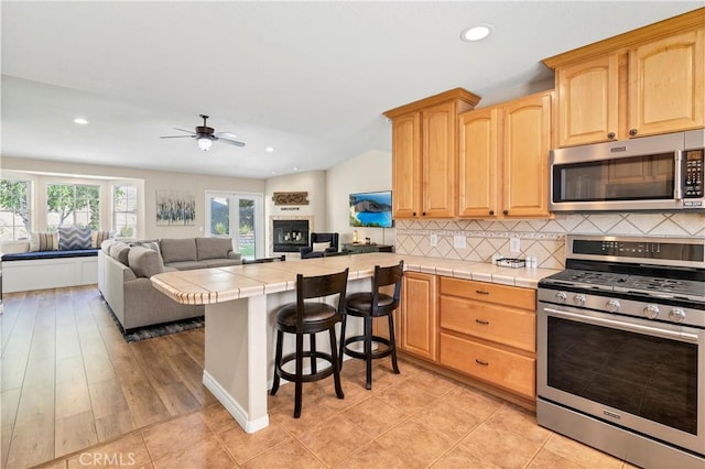 kitchen with appliances with stainless steel finishes, tile countertops, light brown cabinetry, ceiling fan, and recessed lighting