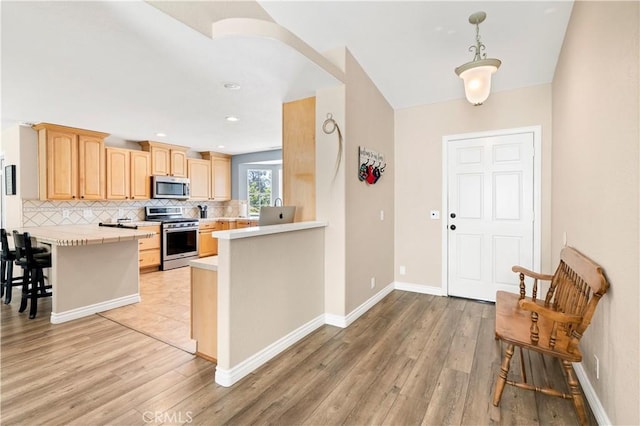 kitchen with stainless steel appliances, a peninsula, light countertops, backsplash, and light wood-style floors