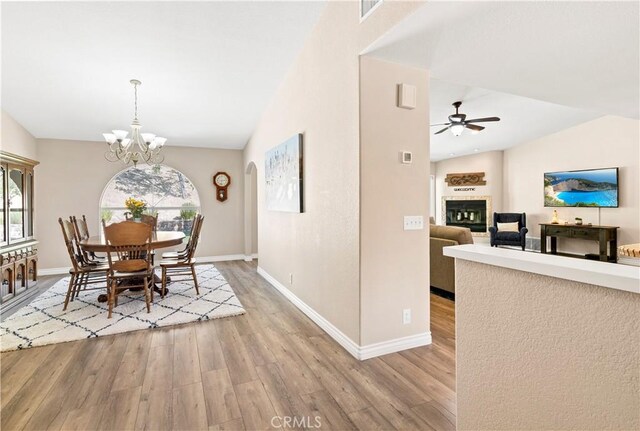 dining space with light wood finished floors, vaulted ceiling, ceiling fan, a glass covered fireplace, and baseboards