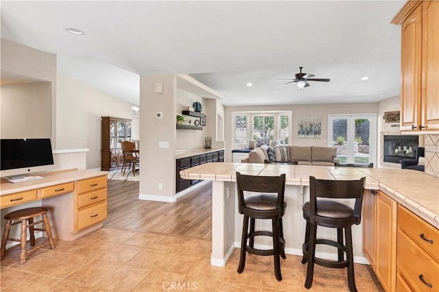 kitchen featuring tile counters, a ceiling fan, open floor plan, a breakfast bar, and a peninsula
