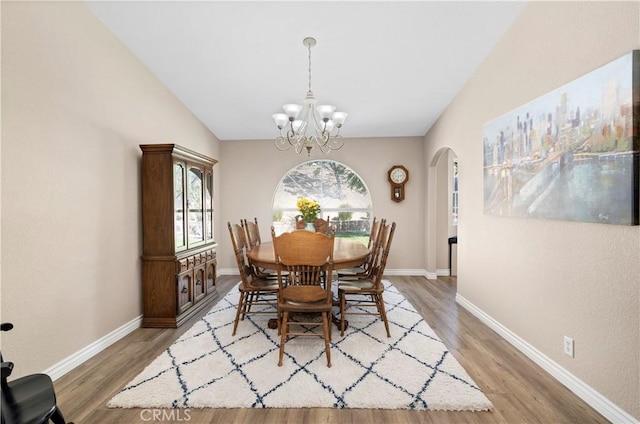 dining room with arched walkways, a chandelier, light wood-style floors, baseboards, and lofted ceiling