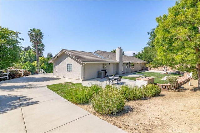 view of property exterior featuring a chimney, a patio, fence, stucco siding, and driveway
