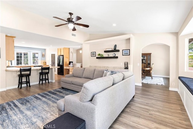 living room featuring arched walkways, lofted ceiling, light wood-style flooring, a ceiling fan, and baseboards