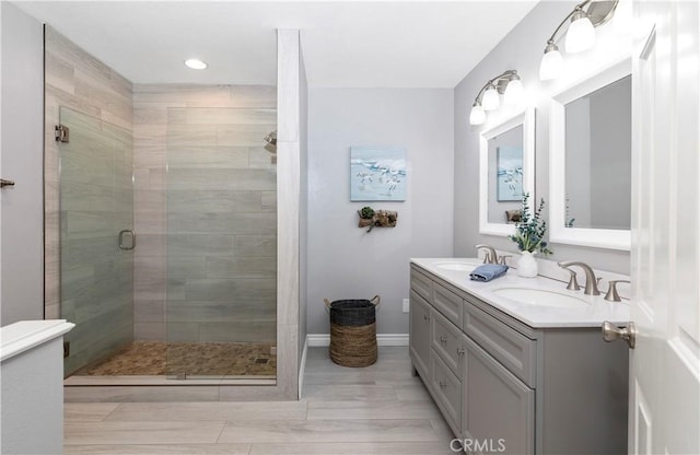 full bathroom with a shower stall, double vanity, baseboards, and recessed lighting