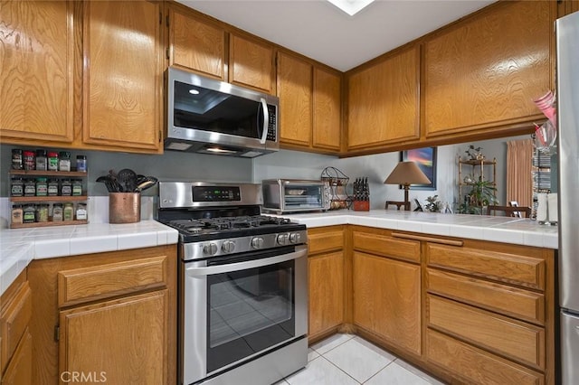 kitchen featuring appliances with stainless steel finishes, a toaster, light tile patterned flooring, and brown cabinetry