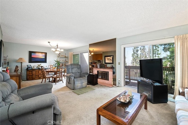 living room with a notable chandelier, light carpet, a glass covered fireplace, and a textured ceiling