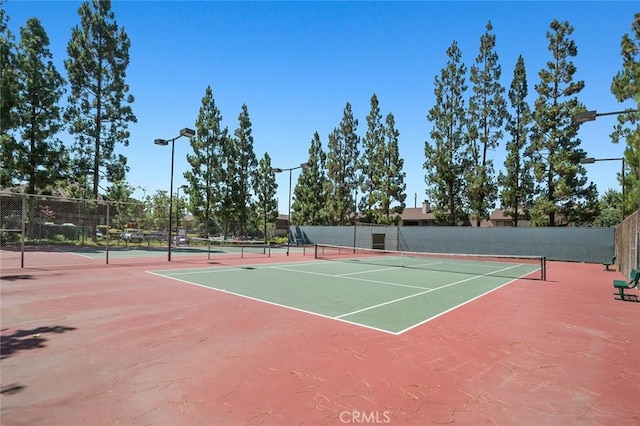 view of tennis court featuring community basketball court and fence