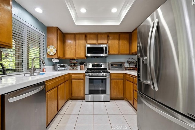 kitchen with brown cabinetry, a raised ceiling, stainless steel appliances, and a sink