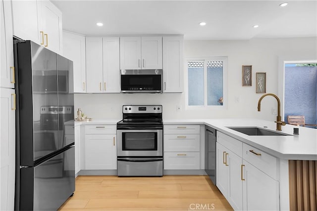 kitchen with a sink, a peninsula, light wood-style floors, light countertops, and appliances with stainless steel finishes
