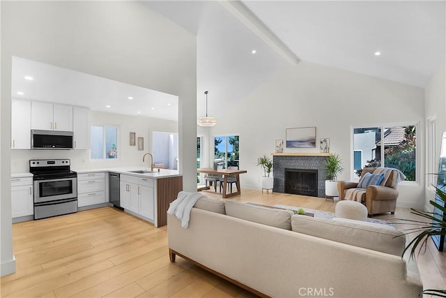 living room with recessed lighting, beam ceiling, a brick fireplace, high vaulted ceiling, and light wood-type flooring