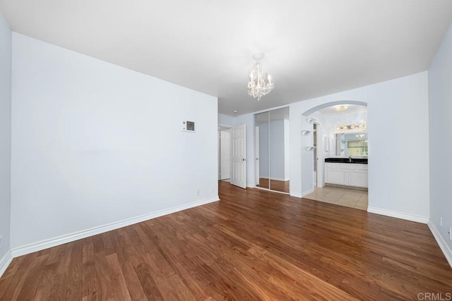 unfurnished living room featuring wood finished floors, baseboards, arched walkways, and a notable chandelier