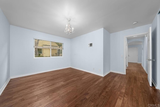 spare room with an inviting chandelier, dark wood finished floors, baseboards, and arched walkways