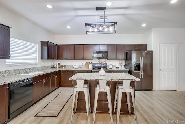 26841 Franklin Ave, Winchester, CA 92596 - kitchen with a kitchen bar, dark brown cabinetry, light wood-type flooring, black appliances, and a kitchen island