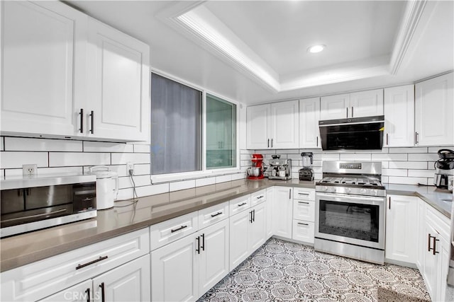 kitchen featuring a tray ceiling, white cabinetry, appliances with stainless steel finishes, and backsplash