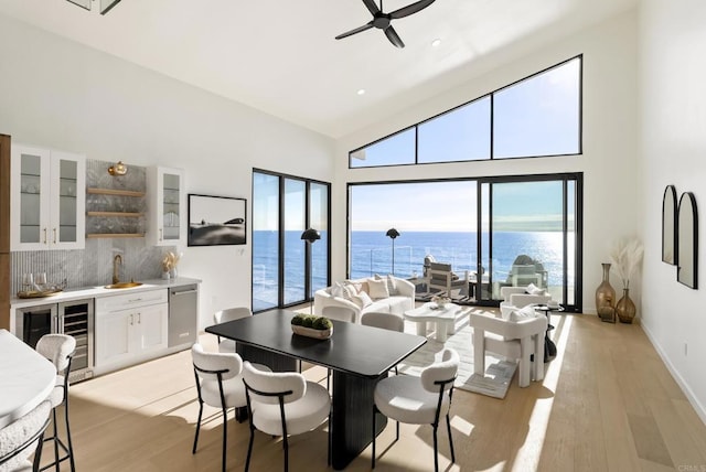 dining space featuring wine cooler, a water view, wet bar, and light wood-type flooring