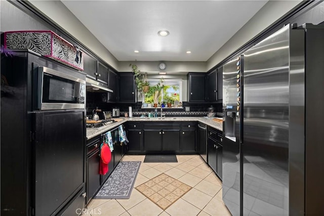 kitchen featuring a sink, under cabinet range hood, decorative backsplash, light tile patterned floors, and appliances with stainless steel finishes