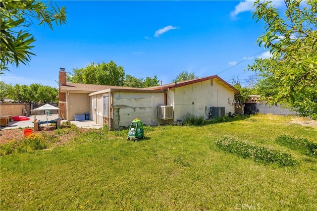 back of house with central AC unit, fence, a chimney, and a lawn