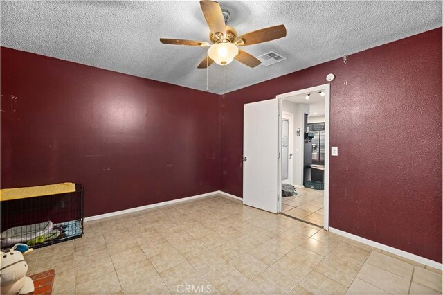 tiled empty room featuring a ceiling fan, a textured ceiling, visible vents, baseboards, and a textured wall