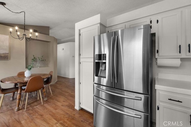 1009 Fairwind Ave, Rosamond, CA 93560 - kitchen with wood finished floors, decorative light fixtures, stainless steel refrigerator with ice dispenser, white cabinets, and a notable chandelier