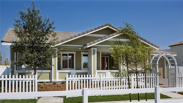 bungalow-style home featuring a porch, a tiled roof, and a fenced front yard