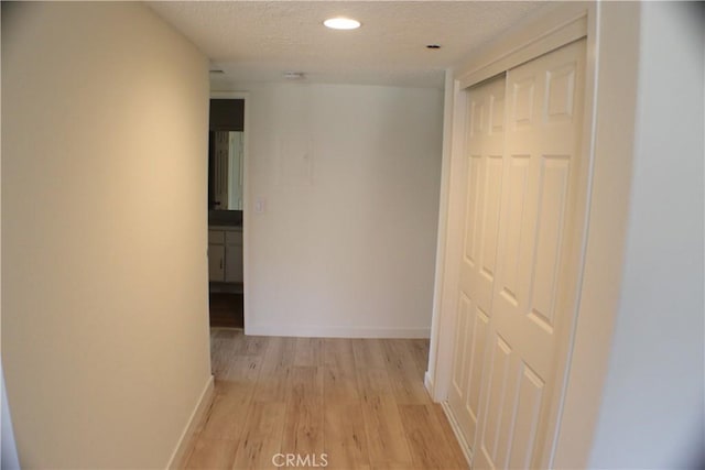 hall featuring light wood finished floors, a textured ceiling, baseboards, and recessed lighting