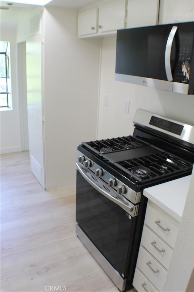 kitchen with light wood finished floors, stainless steel appliances, baseboards, and white cabinets