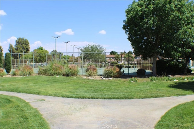 view of home's community with fence, a tennis court, and a lawn