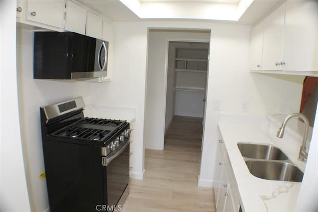 kitchen featuring light wood finished floors, a sink, white cabinetry, gas range, and light countertops