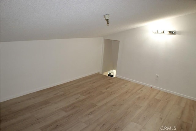 bonus room featuring lofted ceiling, baseboards, light wood-style flooring, and a textured ceiling