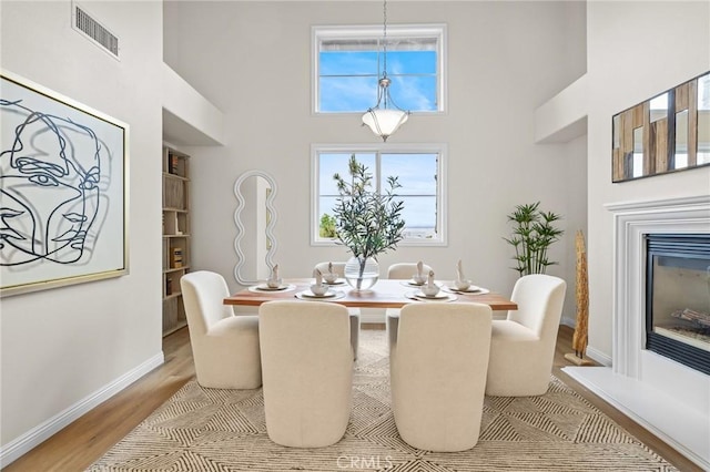 13031 Villosa Pl Unit 437, Playa Vista, CA 90094 - dining space with visible vents, baseboards, a towering ceiling, a glass covered fireplace, and light wood-style floors