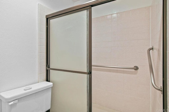 bathroom featuring toilet, a shower stall, and a textured wall