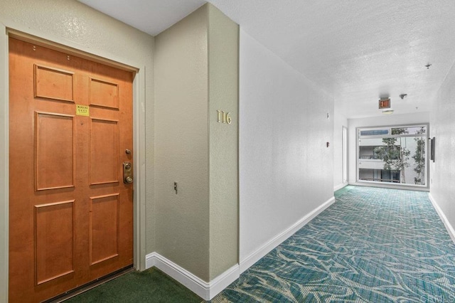 interior space featuring dark colored carpet, a textured wall, baseboards, and a textured ceiling