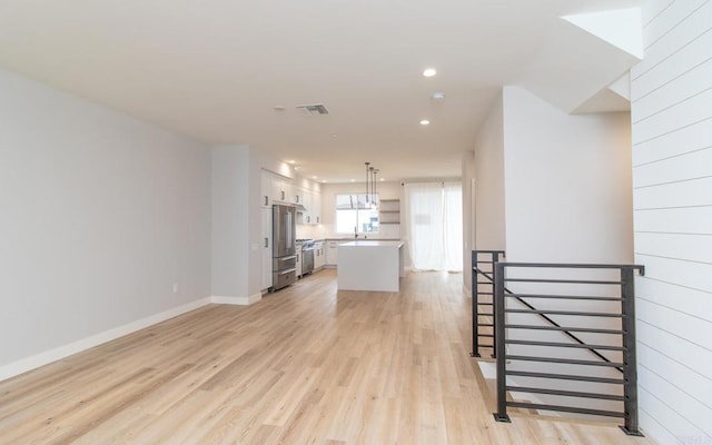 unfurnished living room featuring light wood finished floors, a sink, visible vents, baseboards, and recessed lighting