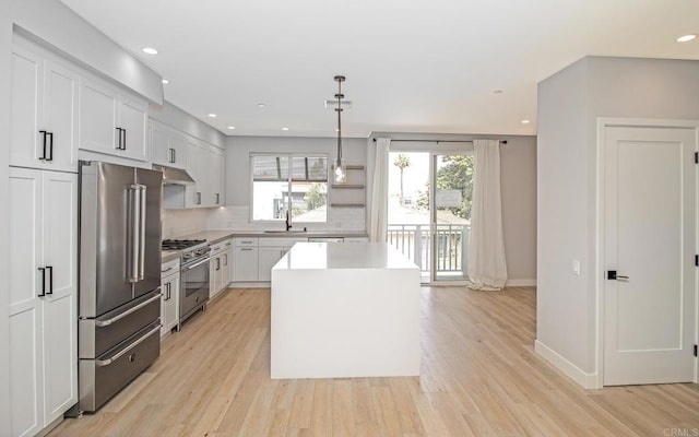 kitchen featuring light wood finished floors, a center island, high end appliances, under cabinet range hood, and tasteful backsplash