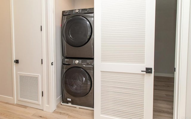 washroom featuring wood finished floors, laundry area, stacked washing maching and dryer, visible vents, and baseboards