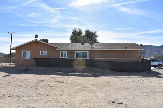 rear view of property with central AC, stucco siding, a mountain view, and fence