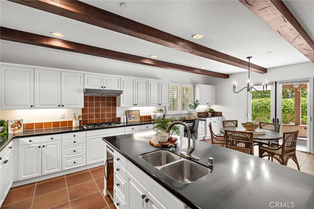 kitchen with a sink, dark countertops, beamed ceiling, stainless steel gas cooktop, and tile patterned floors