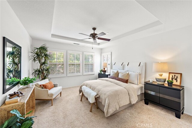 bedroom with a raised ceiling, light colored carpet, and ceiling fan