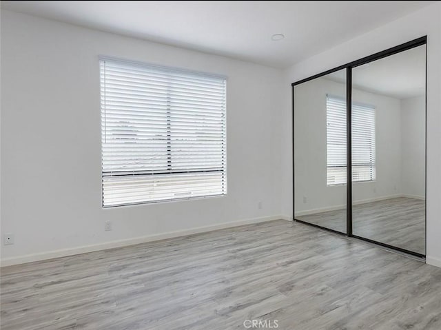 unfurnished bedroom with light wood-style flooring, baseboards, and a closet