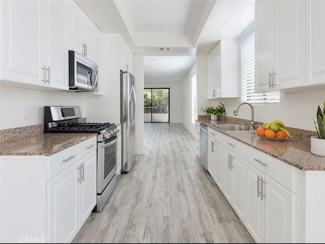 kitchen with stainless steel appliances, a sink, white cabinets, light wood-style floors, and stone countertops
