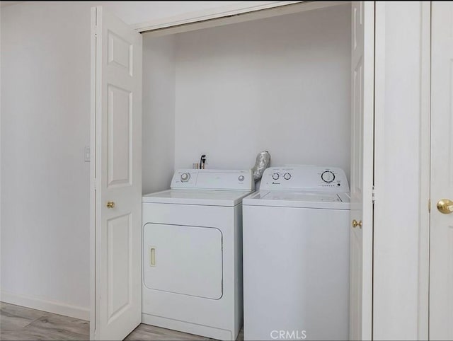 clothes washing area with separate washer and dryer, light wood-type flooring, and baseboards