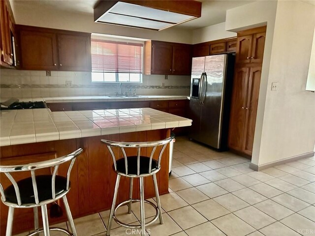 725 18th Pl, Delano, CA 93215 - kitchen featuring a peninsula, a sink, tile counters, stainless steel fridge with ice dispenser, and backsplash