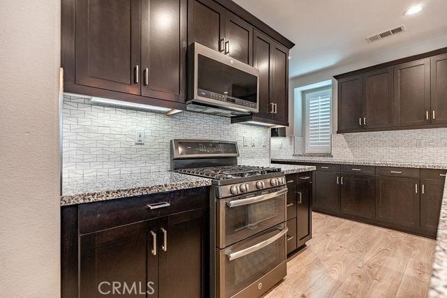24189 Darmera Dr, Lake Elsinore, CA 92532 - kitchen featuring stainless steel appliances, light wood-style floors, light stone counters, and dark brown cabinets