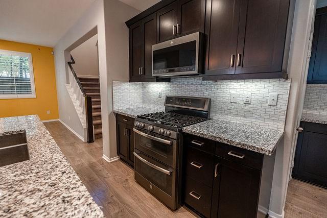 24189 Darmera Dr, Lake Elsinore, CA 92532 - kitchen with appliances with stainless steel finishes, light wood-type flooring, light stone counters, decorative backsplash, and dark brown cabinets